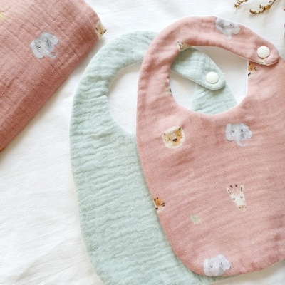 Babetes e saco de bebé em tecido rosa e verde com padrões de animais sobre superfície branca