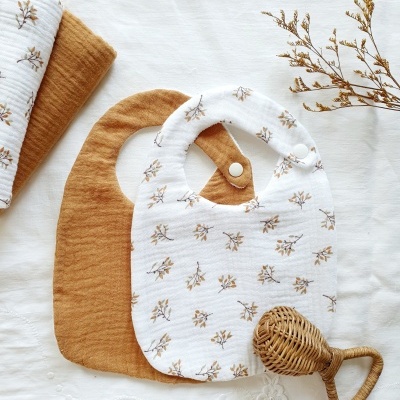 Conjunto de babetes para bebé com padrão floral e chocalho de palha sobre pano branco bordado