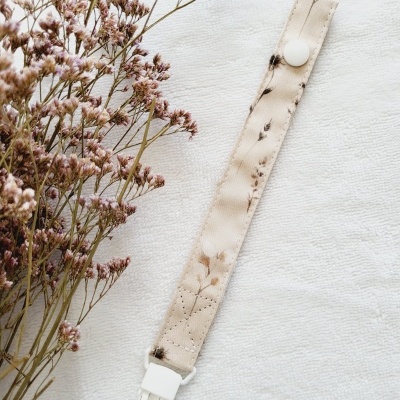 Presilha de tecido floral com fecho branco junto a flores secas