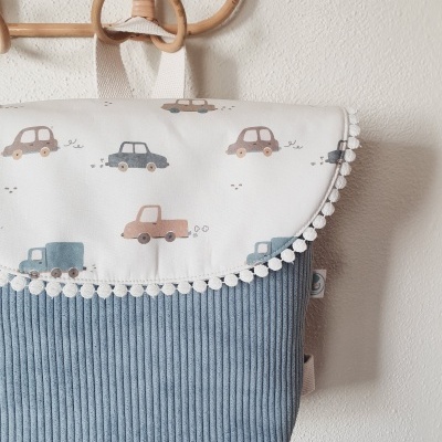 Mochila de tecido com padrão de carros coloridos e pompons pendurada