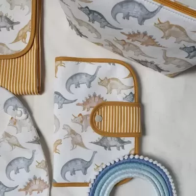 Acessórios para bebé com padrão de dinossauros e detalhes laranja às riscas.