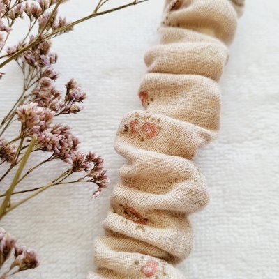 Scrunchie de tecido bege com estampas florais cor-de-rosa e flores secas ao lado