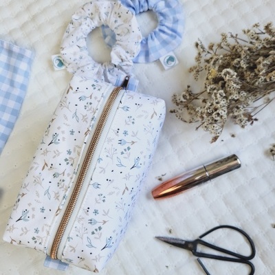 Necessaire floral com scrunchies, batom, tesoura e flores secas num fundo branco acolchoado