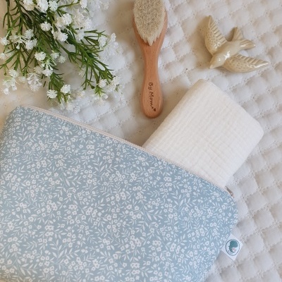 Necessaire azul claro floral, escova de madeira, pano branco e ornamento de pássaro sobre tecido branco