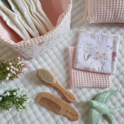 Conjunto para bebé com cesto rosa, fraldas brancas, almofada rosa, panos florais, escova e pente de madeira, flores e passarinho de cerâmica verde