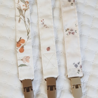 Três fitas de tecido com padrões florais e insectos e fechos de plástico sobre tecido branco acolchoado