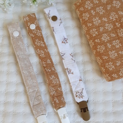 Três prendedores de chupeta tecidos com padrões florais e estojo castanho com padrão branco