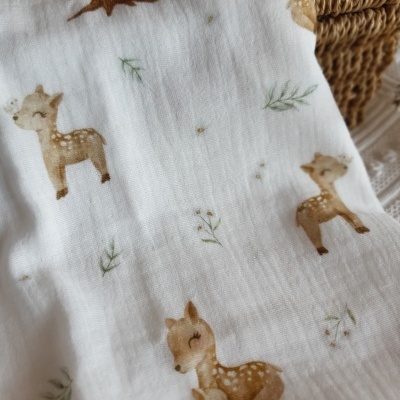 tecido branco com estampado de veados castanhos e ramos verdes ao lado de cesto de fibras naturais