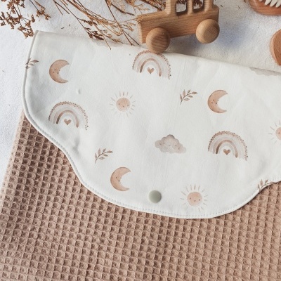 Toalha de tecido bege claro com babete branco estampado e brinquedo de madeira