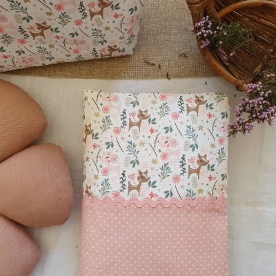 Fronha com padrão de veados e flores em tons pastel e acabamento rosa às bolinhas, com almofadas e cesta de verga