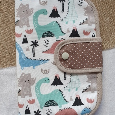 Capa de tecido com padrão de dinossauros coloridos e fecho de botão castanho com bolinhas brancas