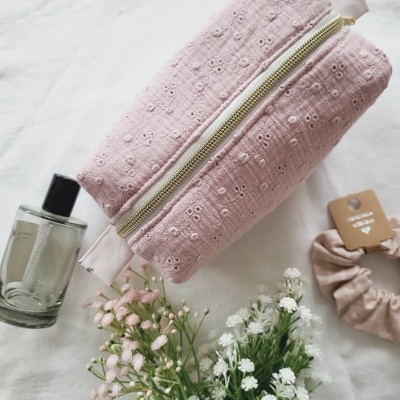 Estojo rosa floral com fecho dourado, frasco de vidro, flores e elástico cor-de-rosa sobre fundo branco.