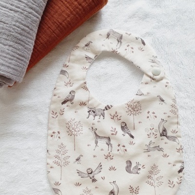 Babete branco com padrão de animais e fecho de pressão, com dois panos ao lado