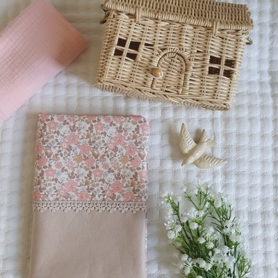 Bolsa em forma de casa de palha, pano floral com renda, pano rosa, figura de pássaro e ramo de flores sobre superfície branca.