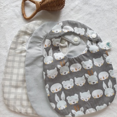 Três babetes para bebé com diferentes padrões e chocalho de vime