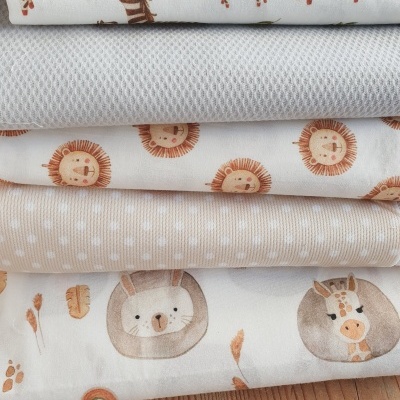 Tecido infantil com estampas de animais e padrão nublado empilhado sobre madeira