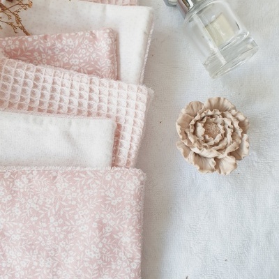 Toalhas rosa e brancas com frasco de vidro e flor decorativa sobre tecido branco