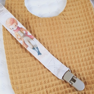 Babete mostarda com padrão nó de mel e fita com desenho de menino loiro