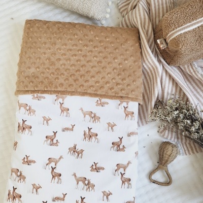 Manta para bebé com padrão de veados e tecido castanho texturizado sobre cama com acessórios