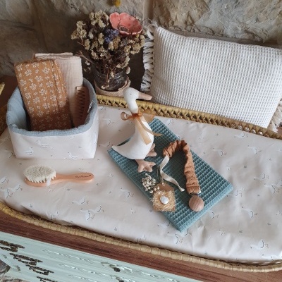 Mesa com almofada e itens decorativos em tecido, madeira e vidro com flores secas em fundo de parede de pedra