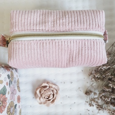 Necessaire rosa canelada com fecho dourado em fundo branco, com padrão floral e flores secas.