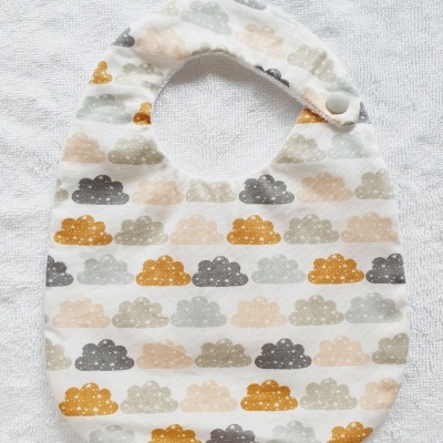 Babete de bebê com padrão de nuvens coloridas e botão branco