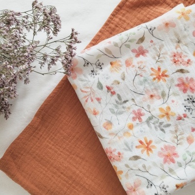 Dois tecidos de algodão, um castanho alaranjado e outro branco com flores, com ramo seco de flores ao lado.