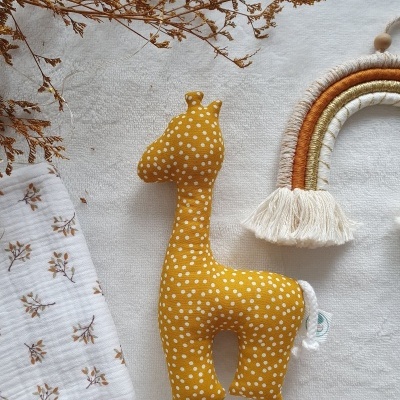 Boneco de girafa em tecido amarelo com bolinhas brancas e arco-íris decorativo ao lado