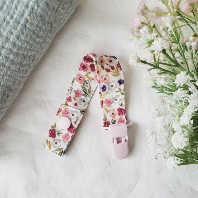 Prendedor para chupeta floral com clip rosa e botão branco sobre tecido branco