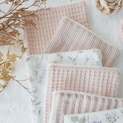 Conjunto de panos de tecido rosa e branco com padrões florais e riscas, dispostos sobre superfície clara com flores secas