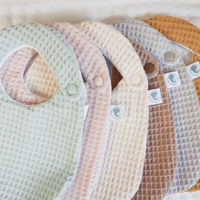 Babetes de pano coloridos com textura de waffle alinhados numa superfície branca