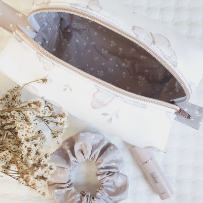 Estojo branco com borboletas, scrunchie cinza floral, planta seca e batom nude