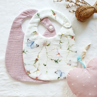Dois babetes de tecido, um floral e outro rosa, com brinquedo em forma de maçã rosa