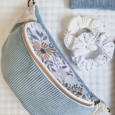 Bolsa azul de veludo cotelê com padrão floral e dois scrunchies sobre fundo branco