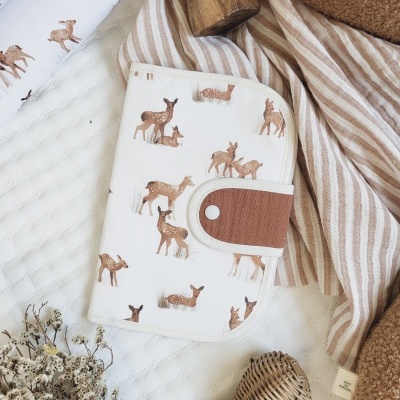 Capa com padrão de veados castanhos em fundo branco com fecho castanho e bege sobre tecidos e flores secas