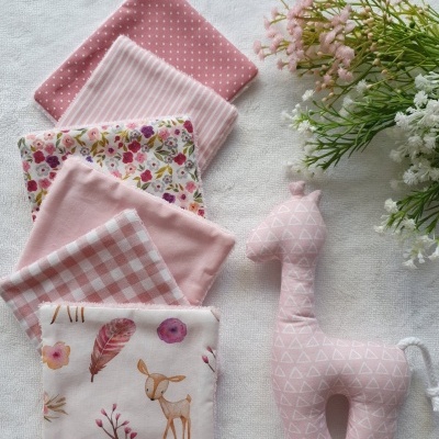 Conjunto de panos de tecido rosa com diferentes padrões e brinquedo de girafa de tecido rosa sobre superfície branca com flores.