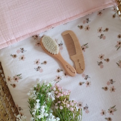 Cama de bebé com lençol de flores, almofada cor-de-rosa, pente e escova de madeira e flores naturais