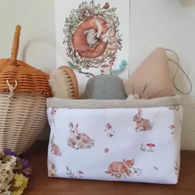 Cesto de tecido branco com padrão de animais castanhos e brinquedos sobre superfície de madeira