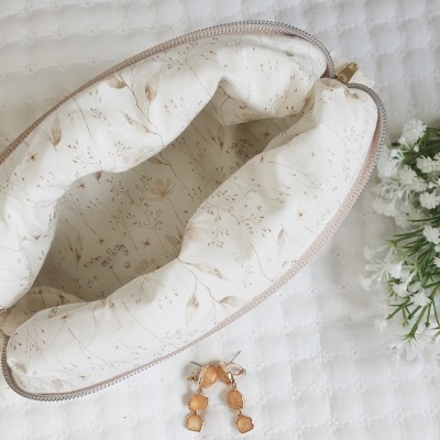 Necessaire branca com padrão de folhas castanhas aberta sobre superfície branca texturada com flores ao lado