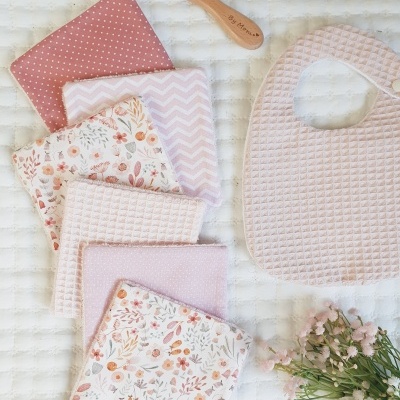 Conjunto de fraldas, babete rosa, escova de madeira e flores sobre superfície branca