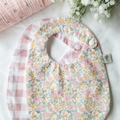 Dois babetes de bebé com padrões florais e de riscas sobre uma superfície branca