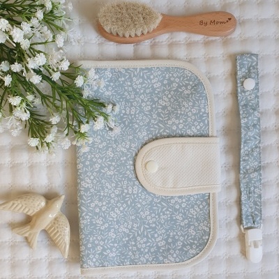Esteira para fraldas azul claro com padrão de folhas, escova de cabelo com cabo de madeira e prendedor de chupeta azul.