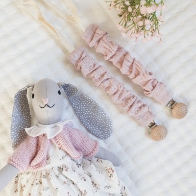 Boneca de coelha de peluche com vestido e casaco rosa, duas fitas de tecido rosa com pregos de madeira, ramo de flores