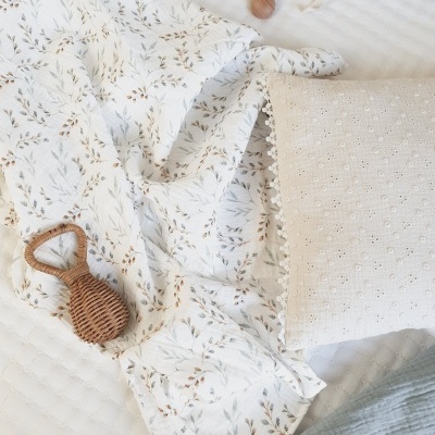 Manta branca com estampado de folhas, almofada creme bordada e acessórios decorativos sobre superfície branca