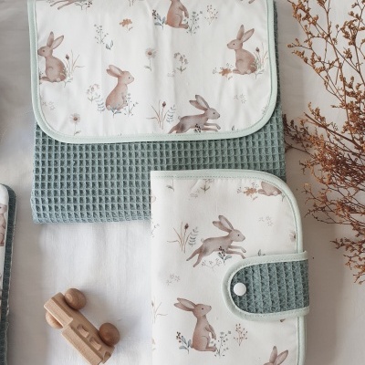 Capas de tecido com padrão de coelhos castanhos e detalhes verde água sobre fundo branco