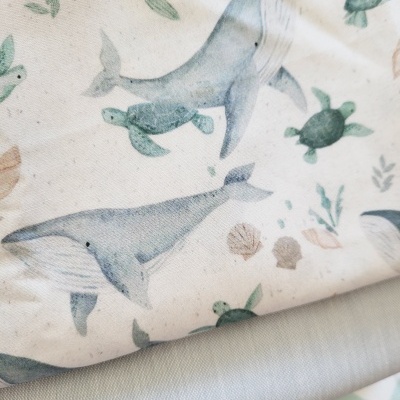 Tecido estampado com baleias, tartarugas e conchas em tons suaves azuis e verdes.