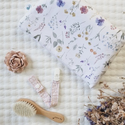 Colcha floral, escova de cabelo de madeira, fita para chupeta rosa, flor decorativa bege e raminhos secos sobre fundo branco texturizado