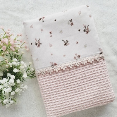 Toalha branca com padrão floral e textura rosa claro com renda sobre superfície cinza claro e flores ao lado