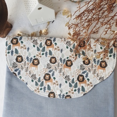 Bolsa de tecido cinzenta com aba estampada de leões e folhas, fecho branco, sobre superfície branca com decoração