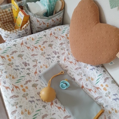 trocador com capa de animais, almofada castanha em forma de coração e acessórios de bebé